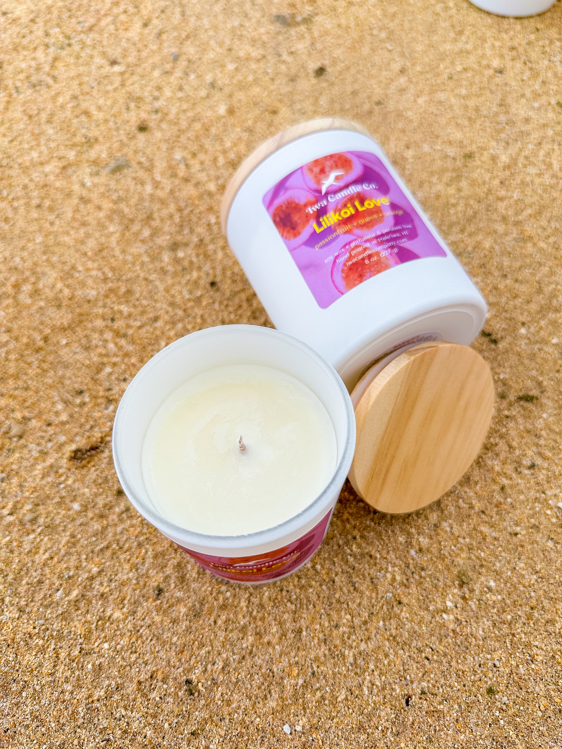 Two candles with wooden lids on a sandy surface
